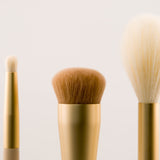 Three makeup brushes with gold handles on a light beige background