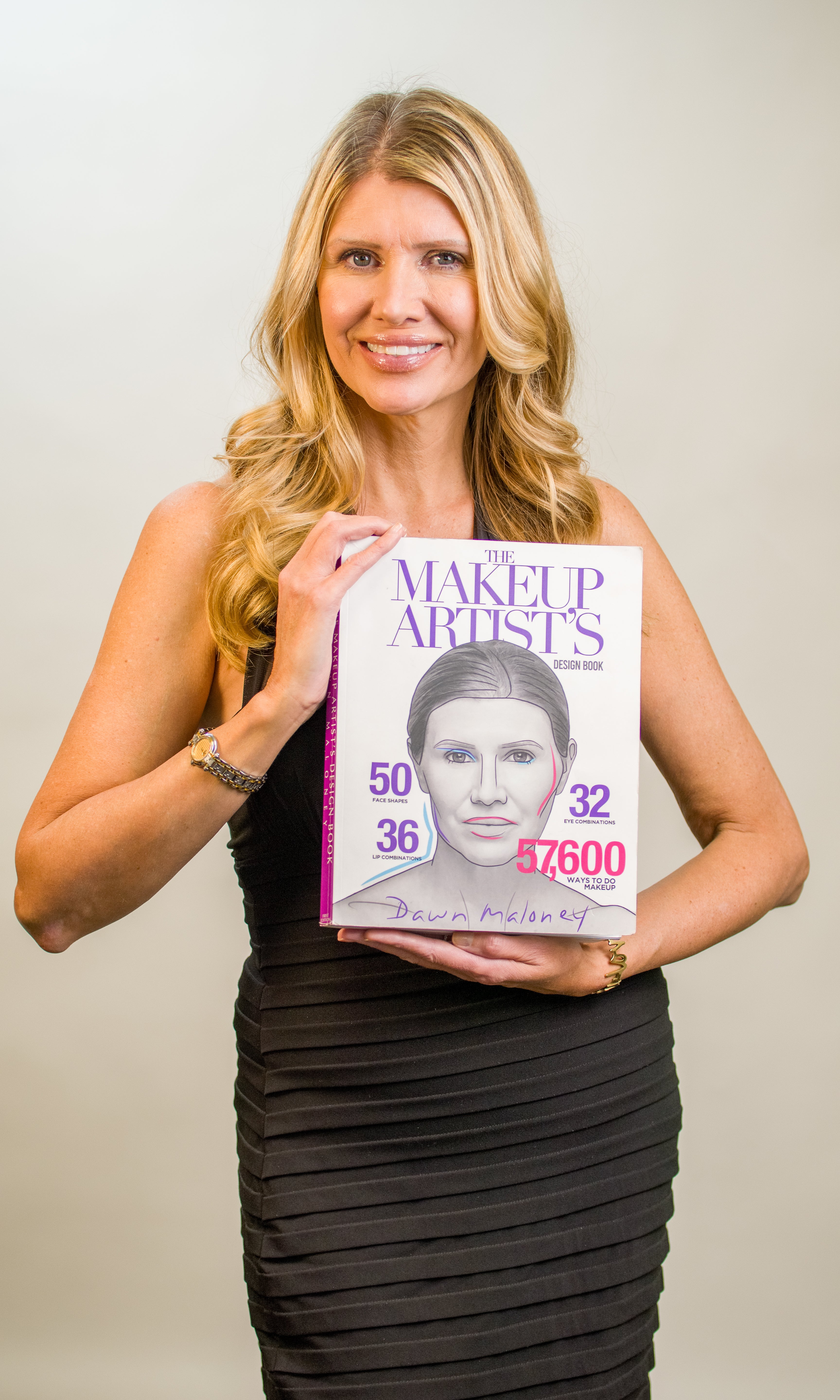 Woman holding a book titled 'The Makeup Artists' Design with a cover featuring a woman's face.