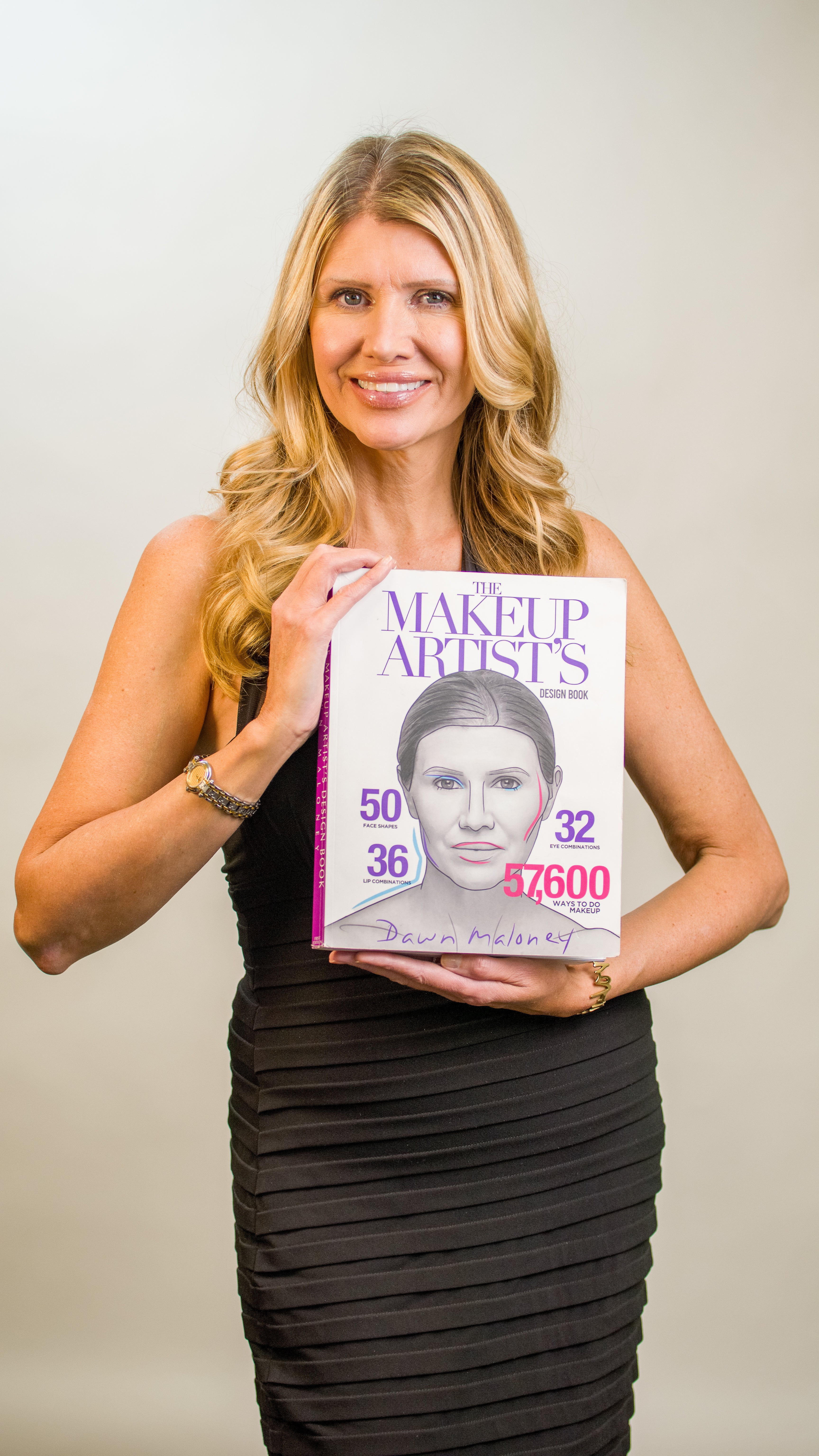 Woman holding a book titled 'The Makeup Artists' Design with a cover featuring a woman's face.