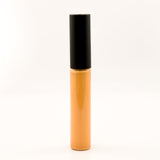 A single cosmetic tube, likely a liquid concealer or lip gloss, standing upright on a seamless white background. The tube is a warm golden-amber color with a black cap.