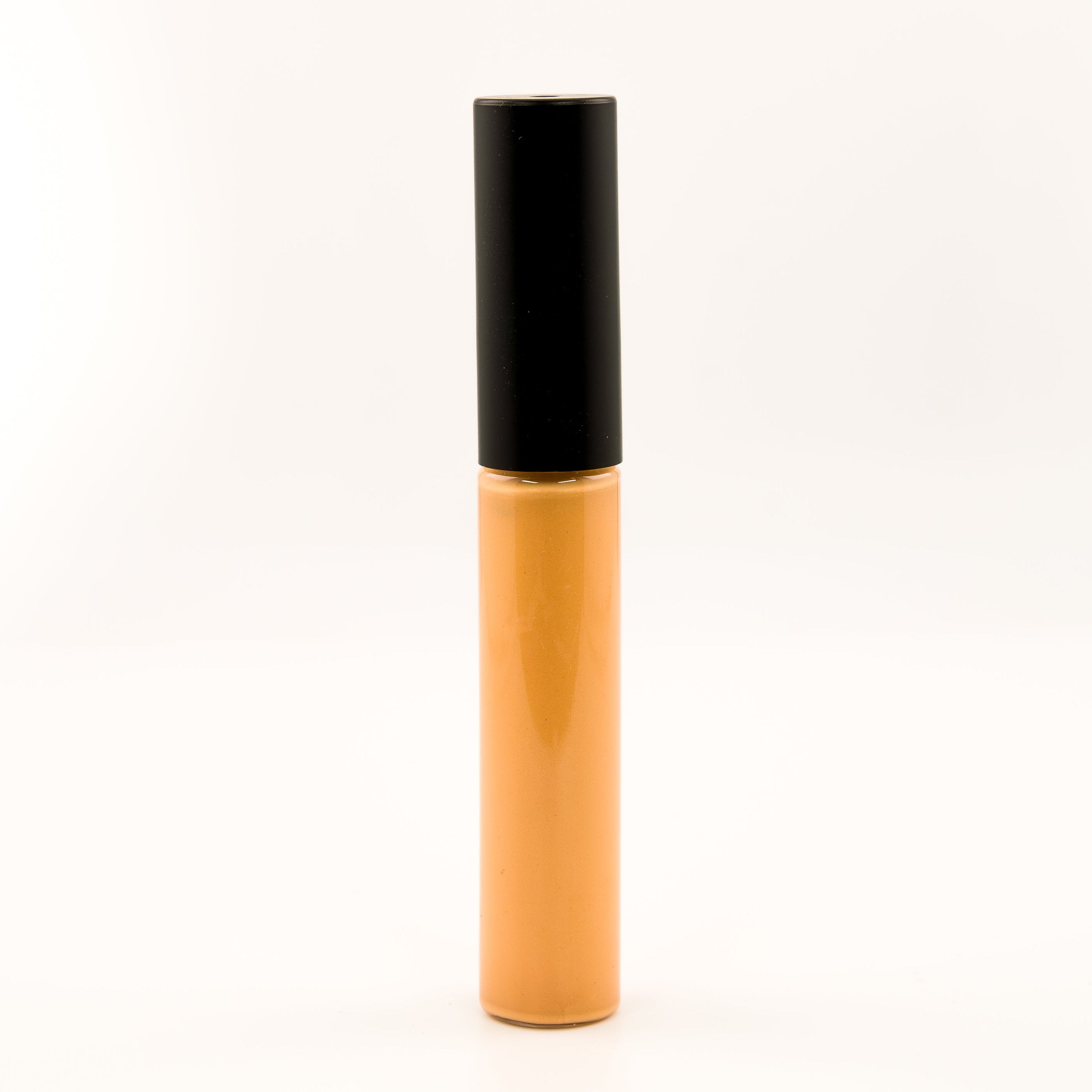 A single cosmetic tube, likely a liquid concealer or lip gloss, standing upright on a seamless white background. The tube is a warm golden-amber color with a black cap.