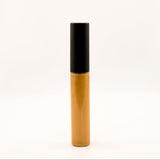 A single cosmetic tube, likely a liquid concealer or lip gloss, standing upright on a seamless white background. The tube has a glossy metallic gold body and a matte black cap.